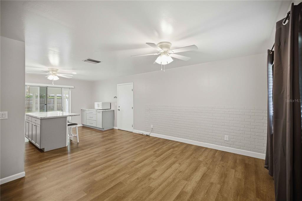 A room with light wood flooring, a white brick accent wall, and a kitchen island — 5207 SE 107TH PLACE, BELLEVIEW, FL