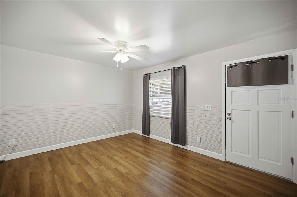 An empty room features white brick walls, wood-look flooring, a ceiling fan, and a door — 5207 SE 107TH PLACE, BELLEVIEW, FL