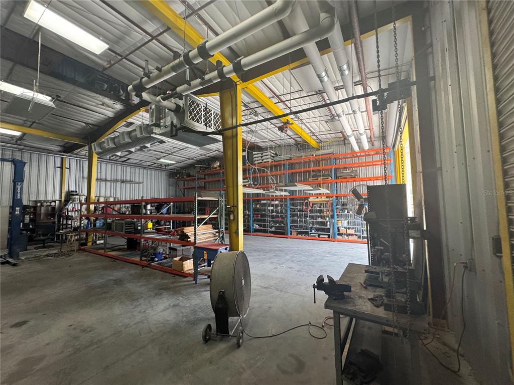 An industrial warehouse space features metal shelving, a concrete floor, and exposed ceiling pipes — 2251 TOPLINE WAY UNIT 2, BROOKSVILLE, FL