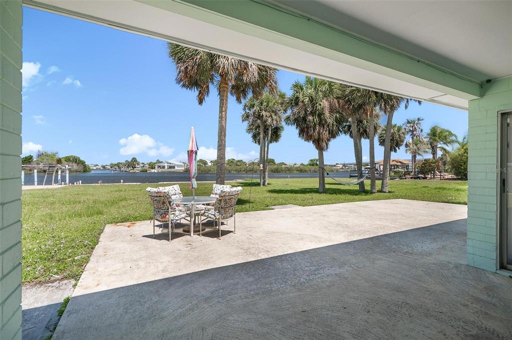 A concrete patio overlooks a grassy lawn, palm trees, and a waterfront canal — 420 LAMBERT AVENUE, FLAGLER BEACH, FL