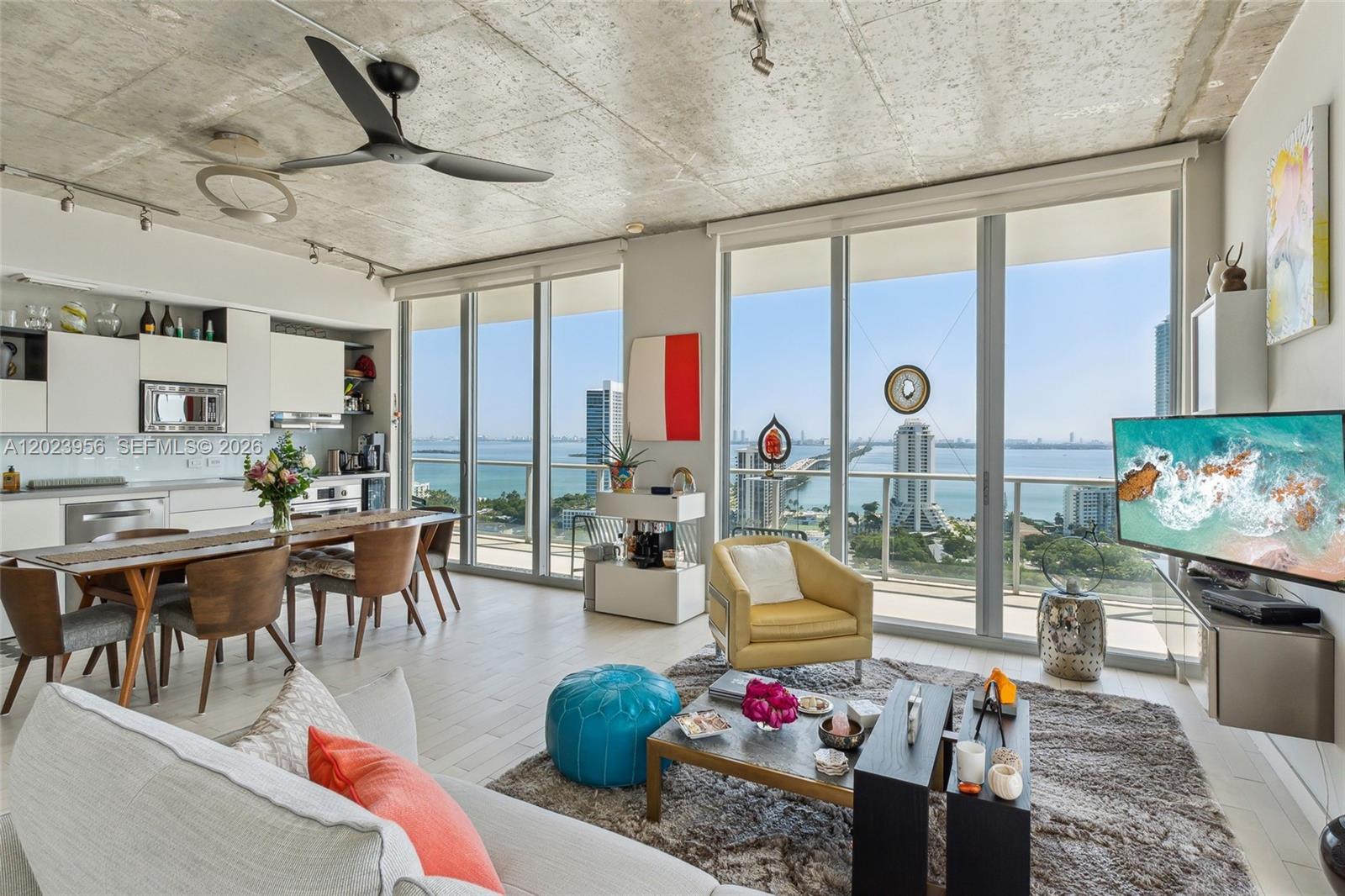 A modern living room and kitchen area features a concrete ceiling, floor-to-ceiling windows, and water views — 3470 E Coast Ave # H2309, Miami FL 33137, MIAMI, FL