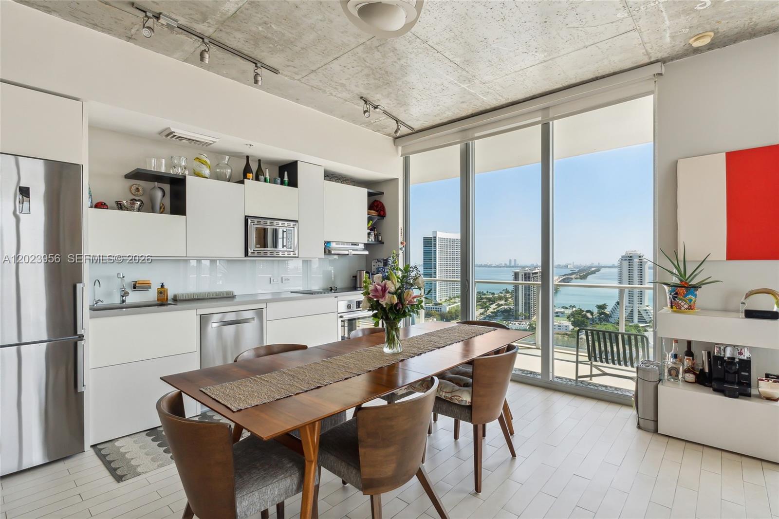 A modern kitchen and dining area with concrete ceilings, white cabinetry, and floor-to-ceiling windows — 3470 E Coast Ave # H2309, Miami FL 33137, MIAMI, FL