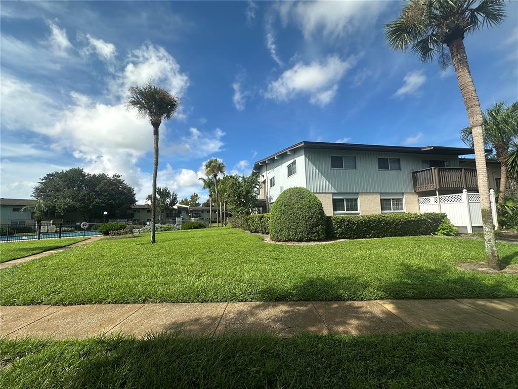 A two-story apartment building sits behind a grassy lawn with palm trees and a pool — 1695 LEE ROAD UNIT E116, WINTER PARK, FL