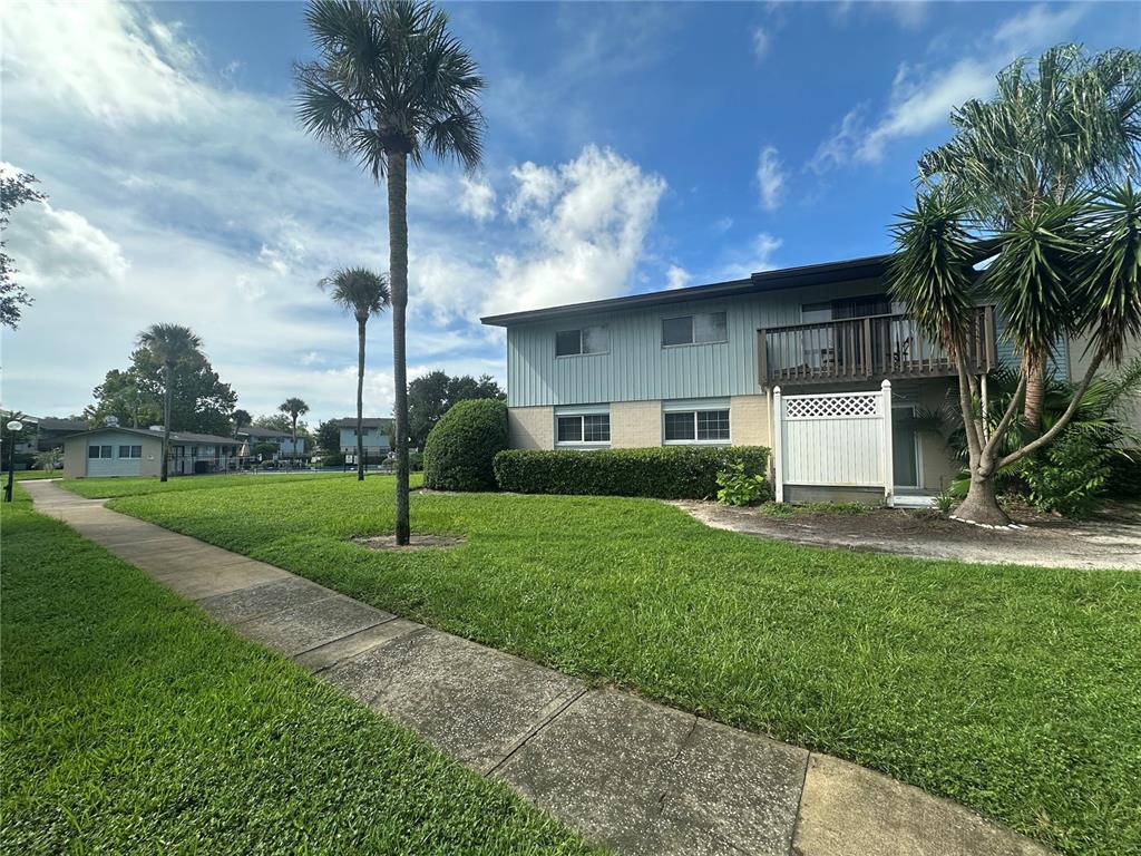 A two-story apartment building with a balcony and palm trees sits beside a concrete walkway — 1695 LEE ROAD UNIT E116, WINTER PARK, FL