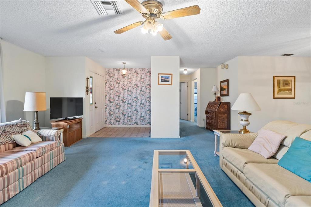 A living room features blue carpeting, a ceiling fan, and a floral wallpapered entryway — 2270 FIRESTONE PLACE, WINTER HAVEN, FL