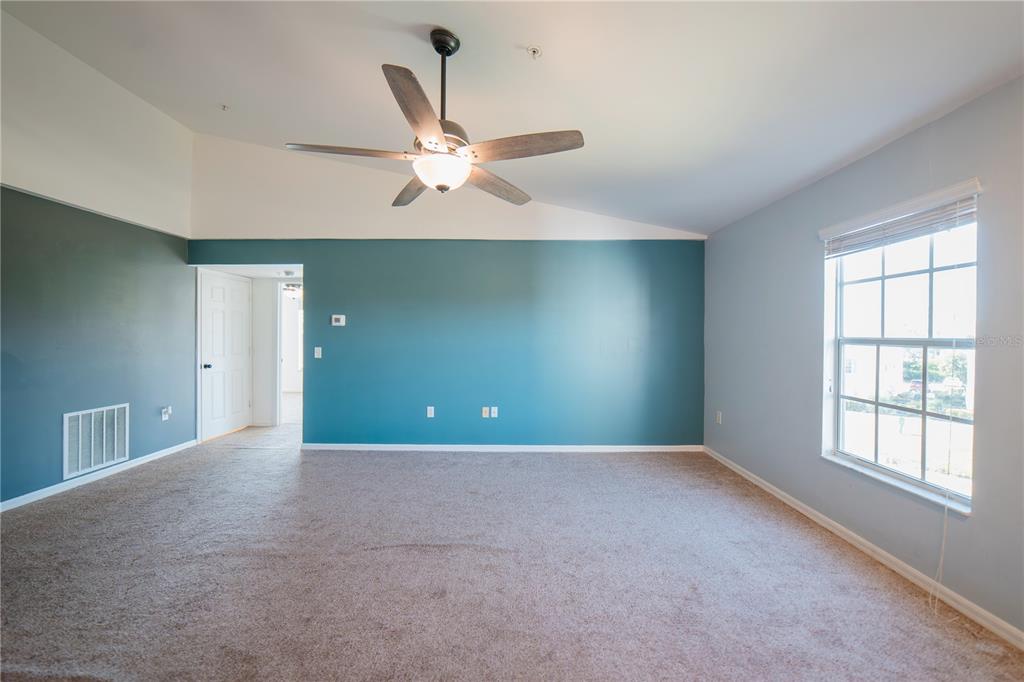 An empty room features teal accent walls, beige carpeting, a ceiling fan, and a window — 1771 FOUR MILE COVE PARKWAY UNIT 1031, CAPE CORAL, FL