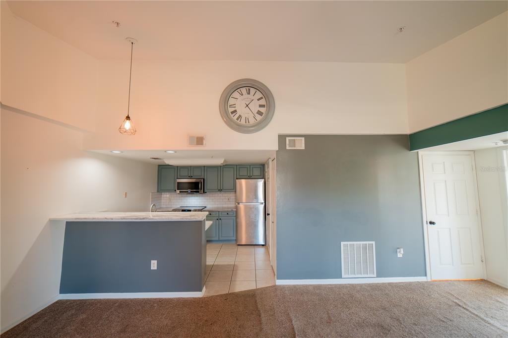 A kitchen with blue cabinets and a breakfast bar overlooks a carpeted living area — 1771 FOUR MILE COVE PARKWAY UNIT 1031, CAPE CORAL, FL