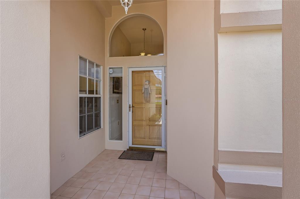 A covered entryway features a tiled floor, a front door with a screen, and a window — 1063 DARTFORD DRIVE, TARPON SPRINGS, FL