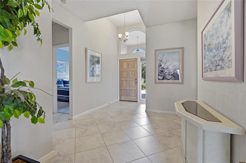 A tiled entryway features a high ceiling, a wooden front door, and a console table — 1063 DARTFORD DRIVE, TARPON SPRINGS, FL
