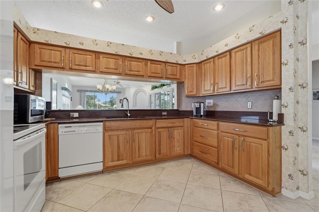 A kitchen with oak cabinets, dark countertops, white appliances, and floral wallpaper above the cabinets — 1063 DARTFORD DRIVE, TARPON SPRINGS, FL