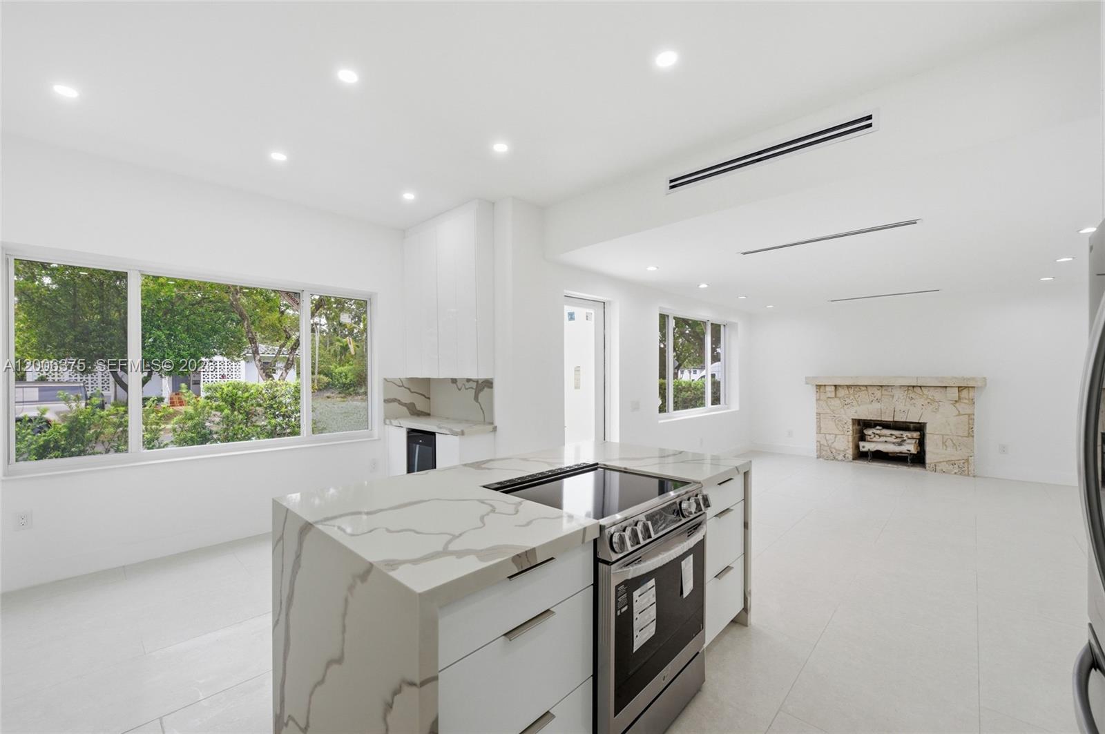 A modern kitchen with a marble waterfall island and stainless steel range overlooks a living area — 5735 SW 12th St, West Miami FL 33144, WEST MIAMI, FL