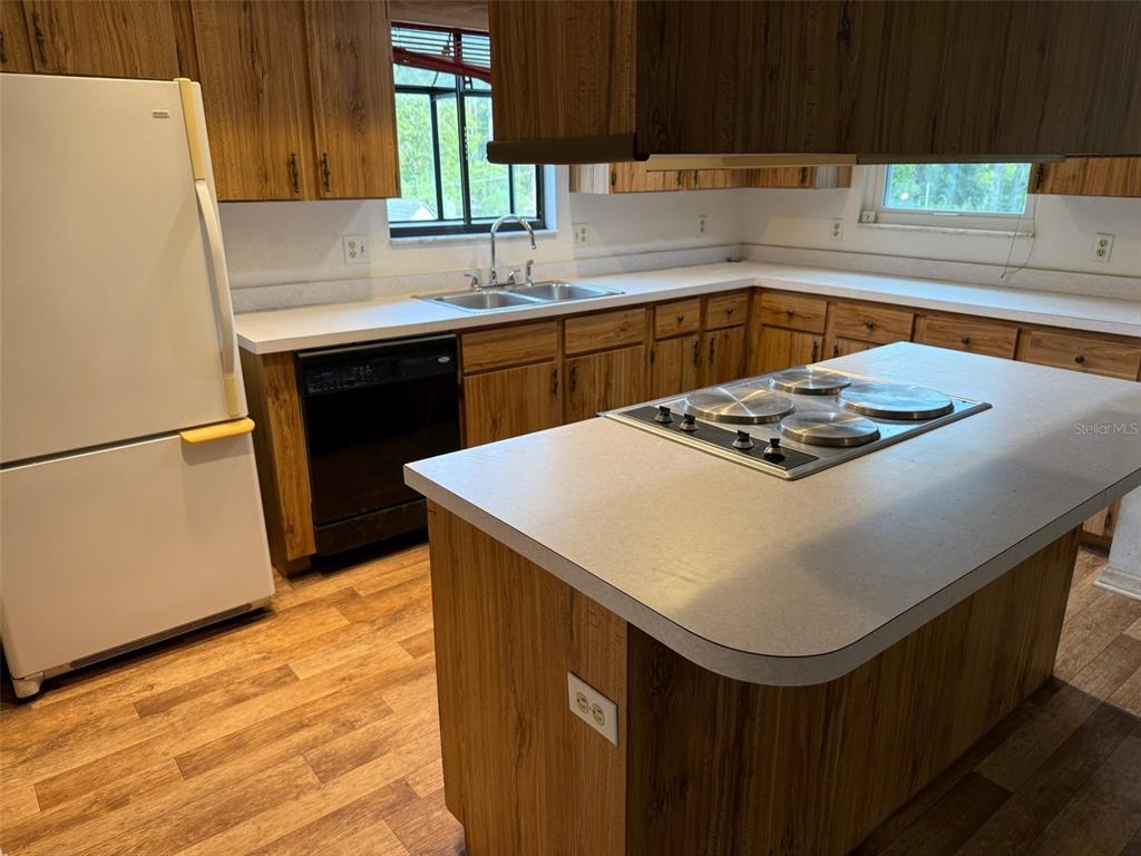 A kitchen features wood cabinets, white countertops, a center island cooktop, and wood-look flooring — 9720 SW 130TH AVENUE, DUNNELLON, FL