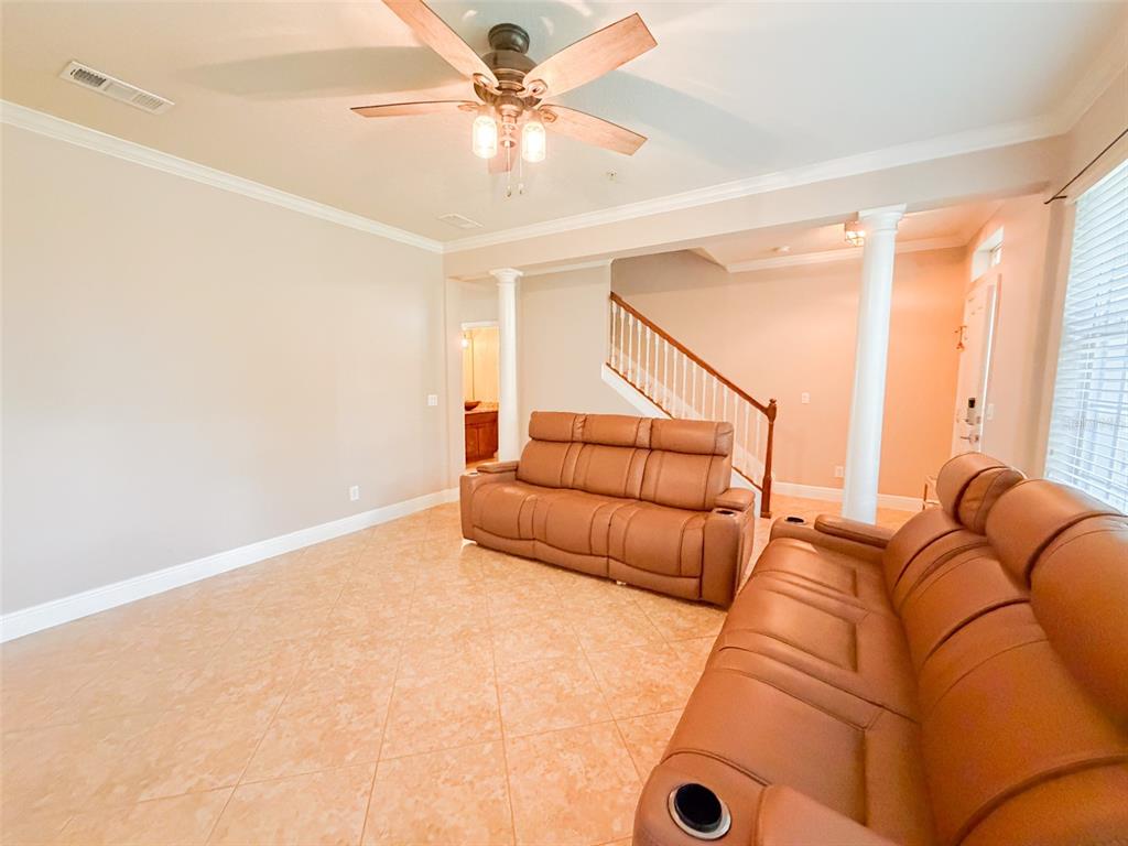 A living room features light tile floors, two brown leather sofas, and a wooden staircase — 5489 BALDWIN PARK STREET, ORLANDO, FL