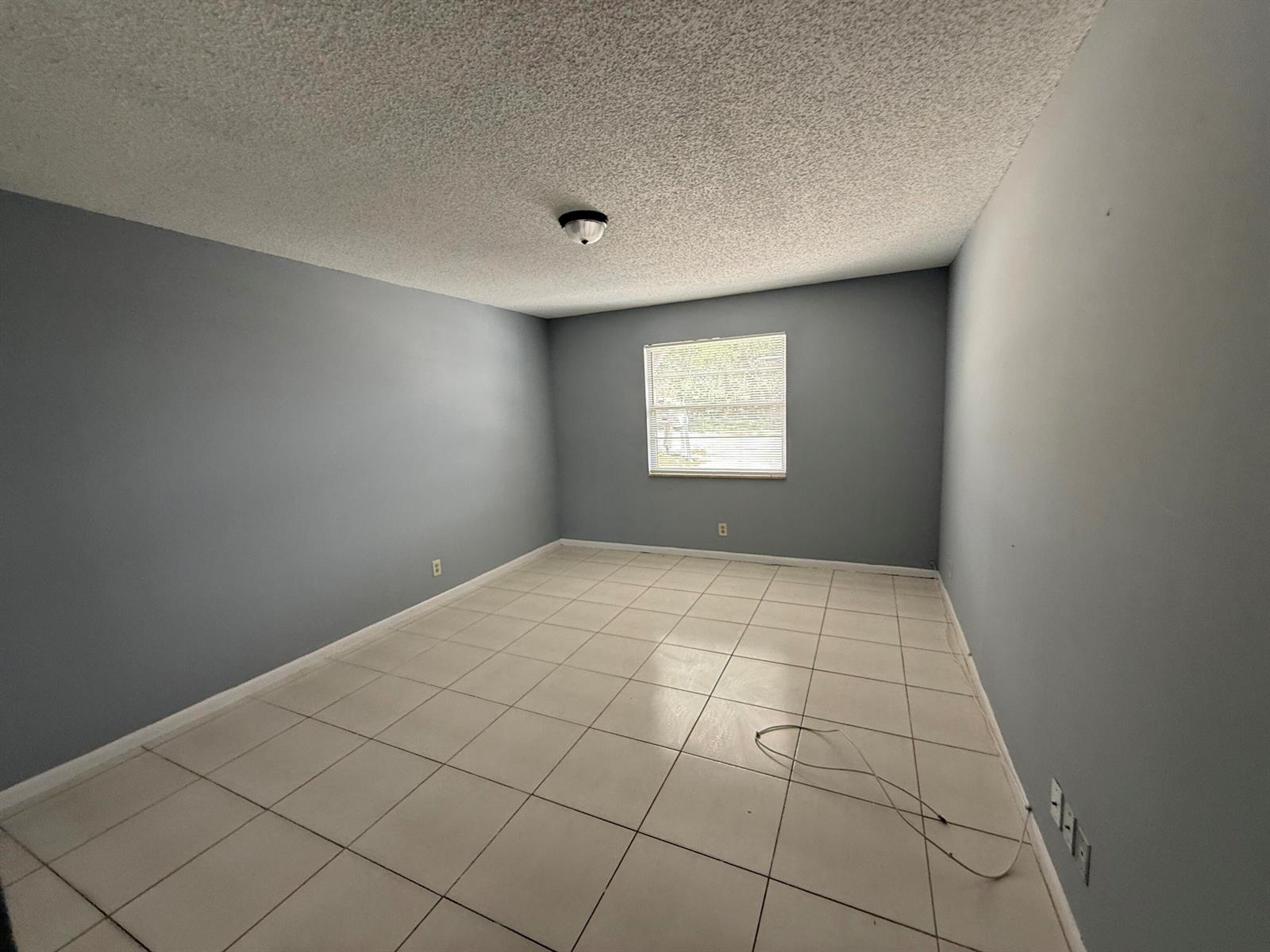 An empty room features gray walls, white tile flooring, and a popcorn ceiling — 2519 Griffin Square, FL 33406, FL