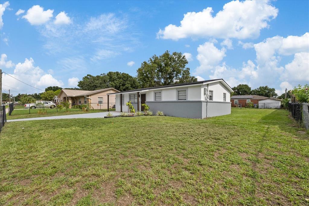 A white and gray single-story house sits on a large, grassy lot under a blue sky — 8303 BAHIA AVENUE, TAMPA, FL