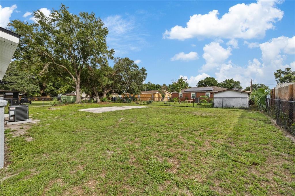 A grassy backyard features a concrete pad, mature trees, and a detached shed — 8303 BAHIA AVENUE, TAMPA, FL
