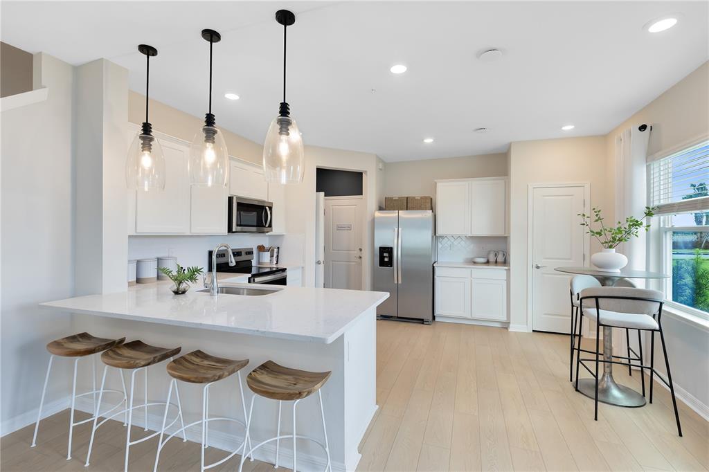 A modern kitchen features white cabinets, quartz countertops, a center island, and light wood flooring — 5115 MORNING DEW LANE, WEST MELBOURNE, FL