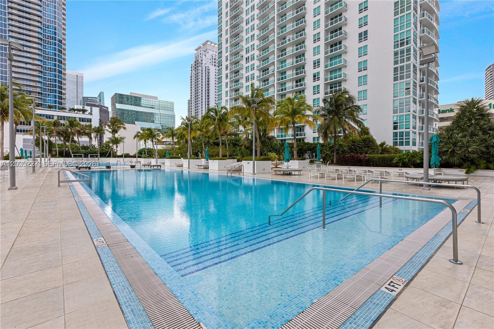 A rectangular outdoor swimming pool with steps and metal railings is surrounded by a tiled deck — 951 BRICKELL AV # 3401, Miami FL 33131, MIAMI, FL