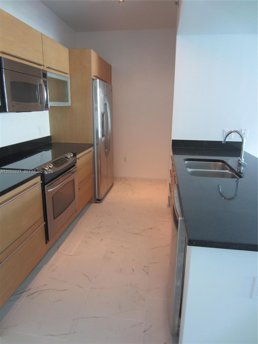A galley kitchen features light wood cabinets, black countertops, stainless steel appliances, and marble flooring — 951 BRICKELL AV # 3401, Miami FL 33131, MIAMI, FL
