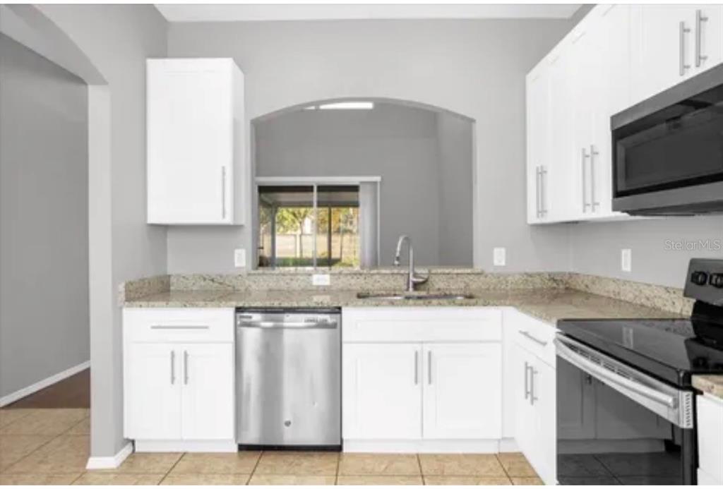 A kitchen with white cabinets, granite countertops, stainless steel appliances, and an arched pass-through window — 13180 SUMMERTON DRIVE, ORLANDO, FL