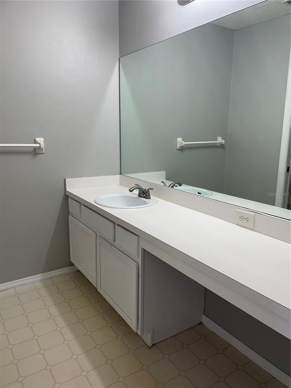 A bathroom vanity with a white countertop, single sink, and large mirror against gray walls — 13180 SUMMERTON DRIVE, ORLANDO, FL