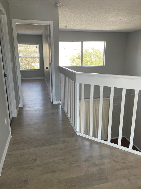 A hallway with wood-look flooring leads to a bedroom past a white staircase railing — 13180 SUMMERTON DRIVE, ORLANDO, FL