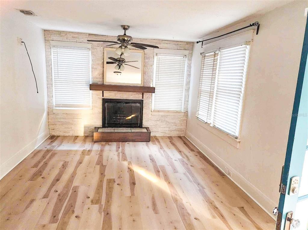 A living room features a stone fireplace, wood-look flooring, and windows with white blinds — 503 W IDLEWILD AVENUE, TAMPA, FL
