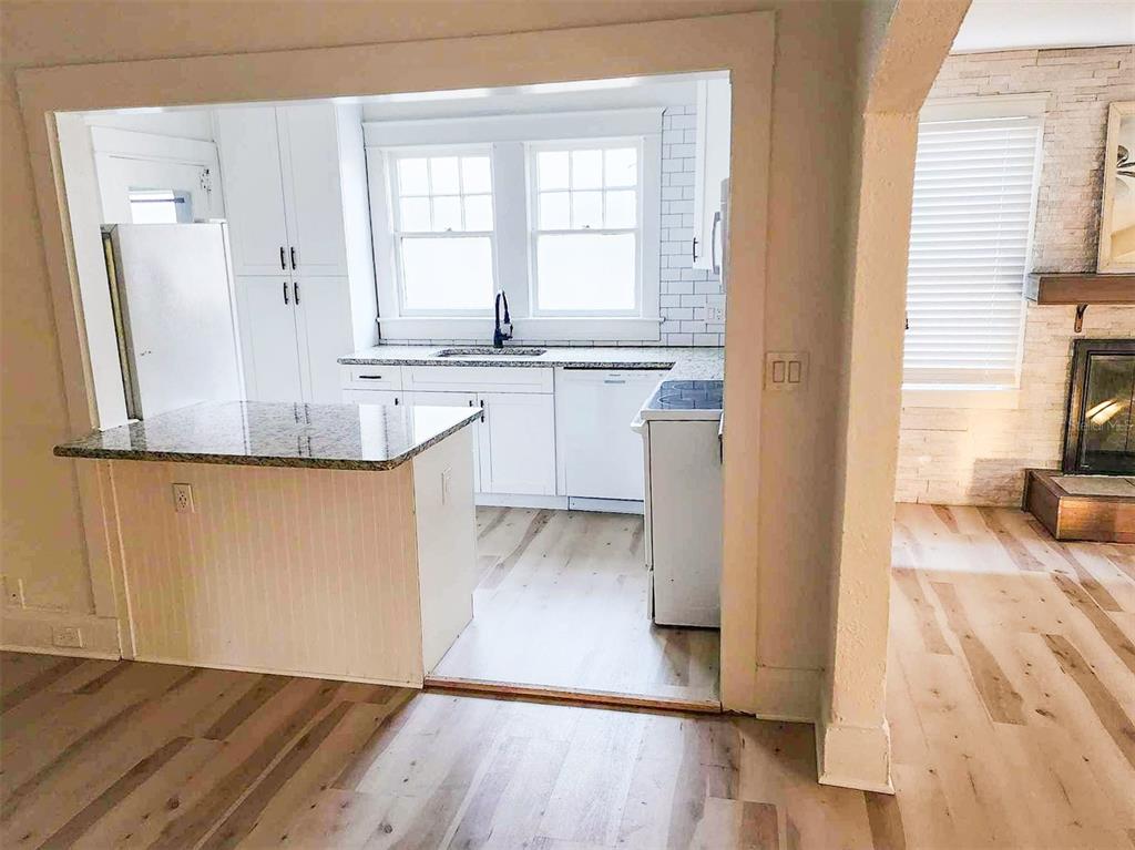 A kitchen with white cabinets, granite countertops, and light wood flooring opens to a living area — 503 W IDLEWILD AVENUE, TAMPA, FL