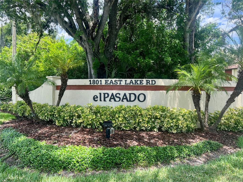 A stucco monument sign for a residential community sits behind a landscaped garden bed — 1801 E LAKE ROAD UNIT 17C, PALM HARBOR, FL