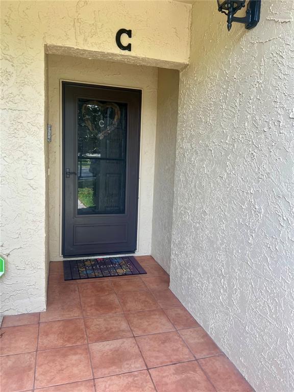A dark brown front door with a storm door sits under a letter C sign — 1801 E LAKE ROAD UNIT 17C, PALM HARBOR, FL