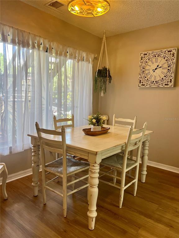 A dining room features a white wooden table, four chairs, sheer curtains, and a wall clock — 1801 E LAKE ROAD UNIT 17C, PALM HARBOR, FL