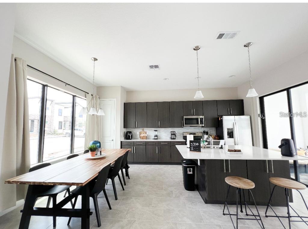 A modern kitchen and dining area with dark wood cabinetry, a large island, and tile flooring — 175 VILLA DOMANI CIRCLE, DAVENPORT, FL