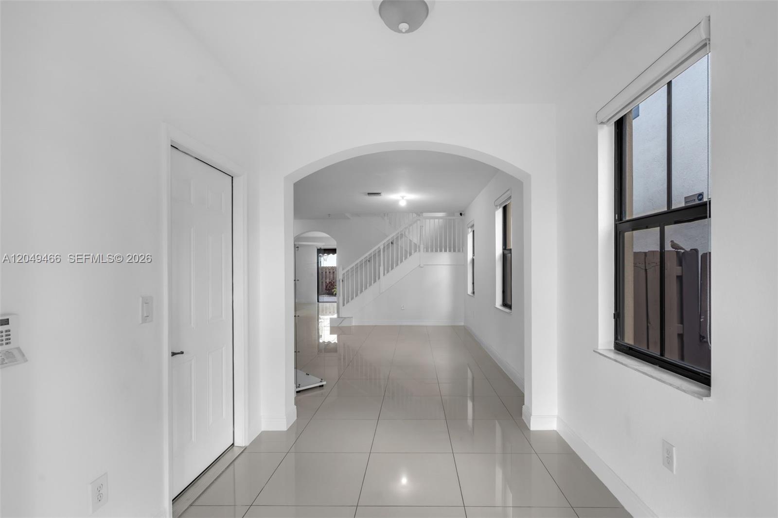 A bright entryway with white walls, tile flooring, an arched opening, and a staircase — 8850 NW 99th Path, Doral FL 33178, DORAL, FL
