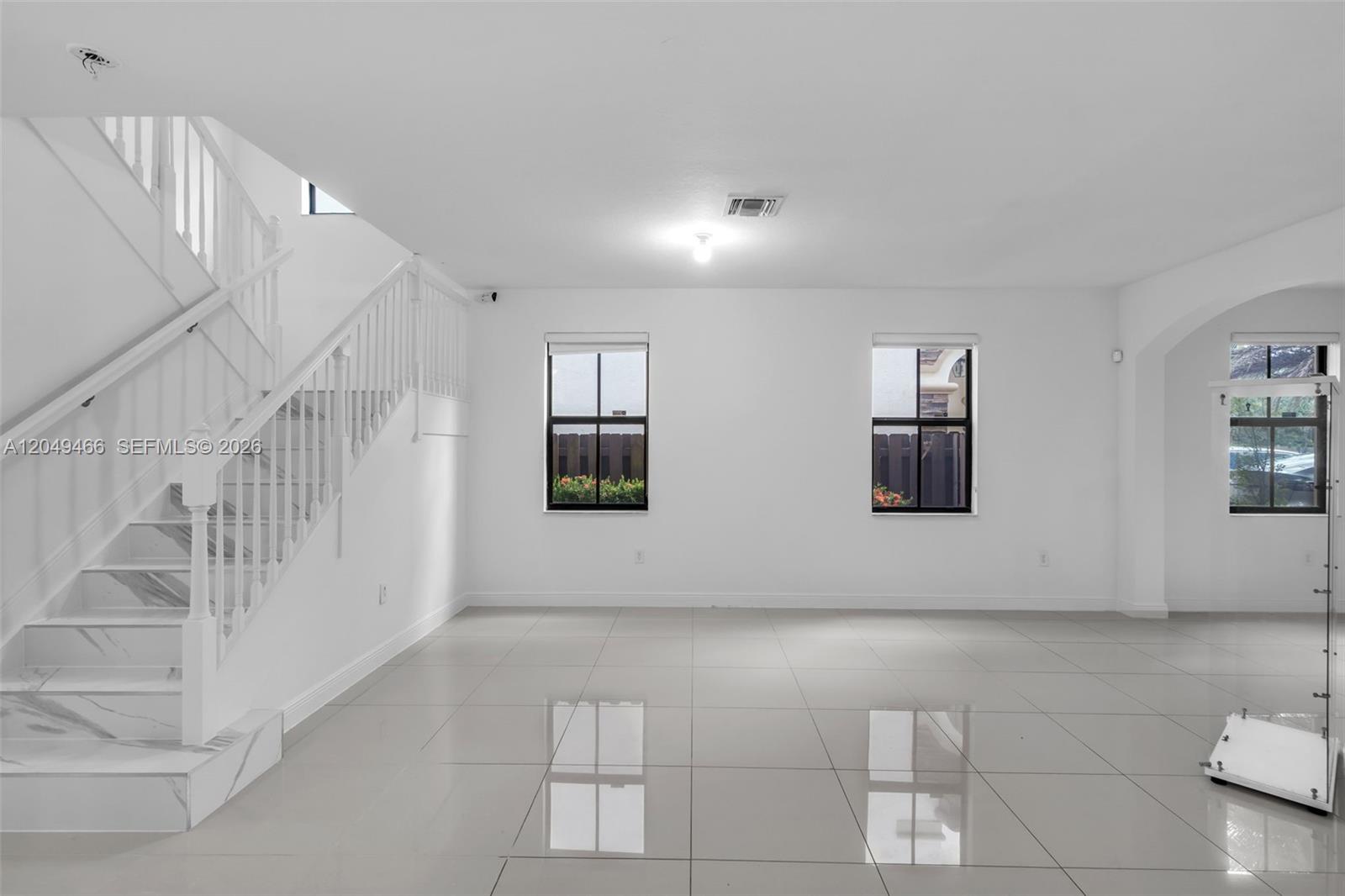 A bright, empty room features white walls, large tile flooring, and a white staircase — 8850 NW 99th Path, Doral FL 33178, DORAL, FL
