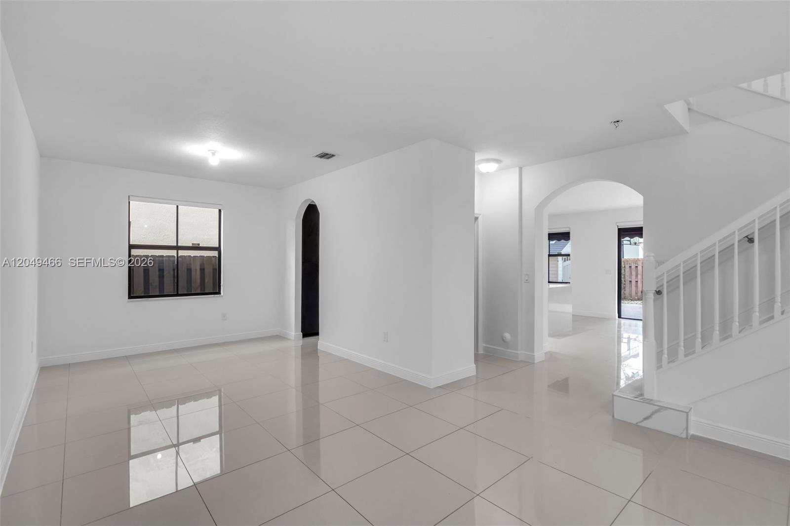 A bright, empty living room features white walls, large light-colored floor tiles, and a staircase — 8850 NW 99th Path, Doral FL 33178, DORAL, FL