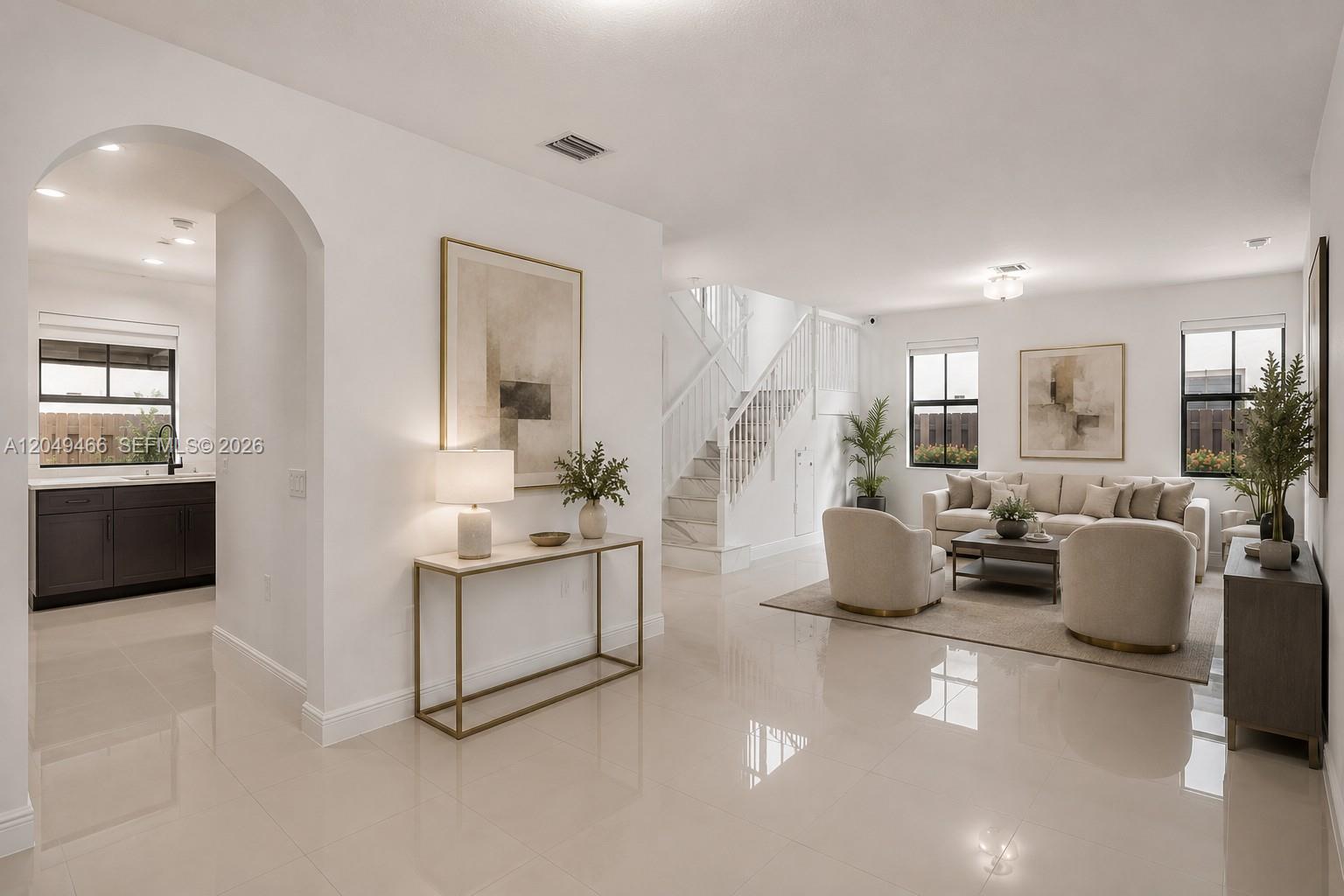 A bright, open-concept living room features white tile floors, a staircase, and adjacent kitchen area — 8850 NW 99th Path, Doral FL 33178, DORAL, FL