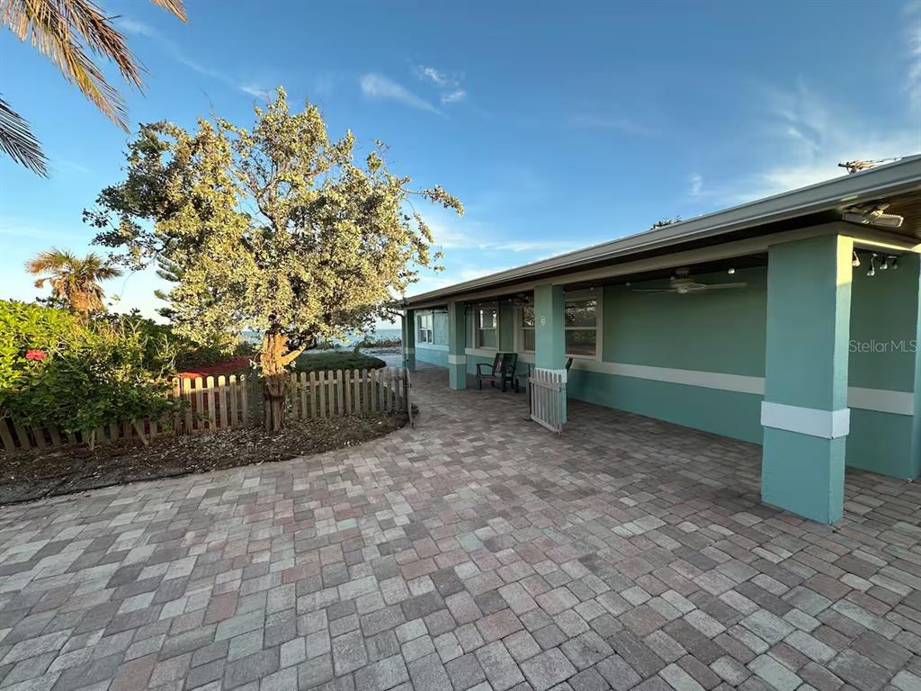 A paved patio area sits beside a teal house with a wooden fence and tree — 5 PARK AVENUE, SATELLITE BEACH, FL
