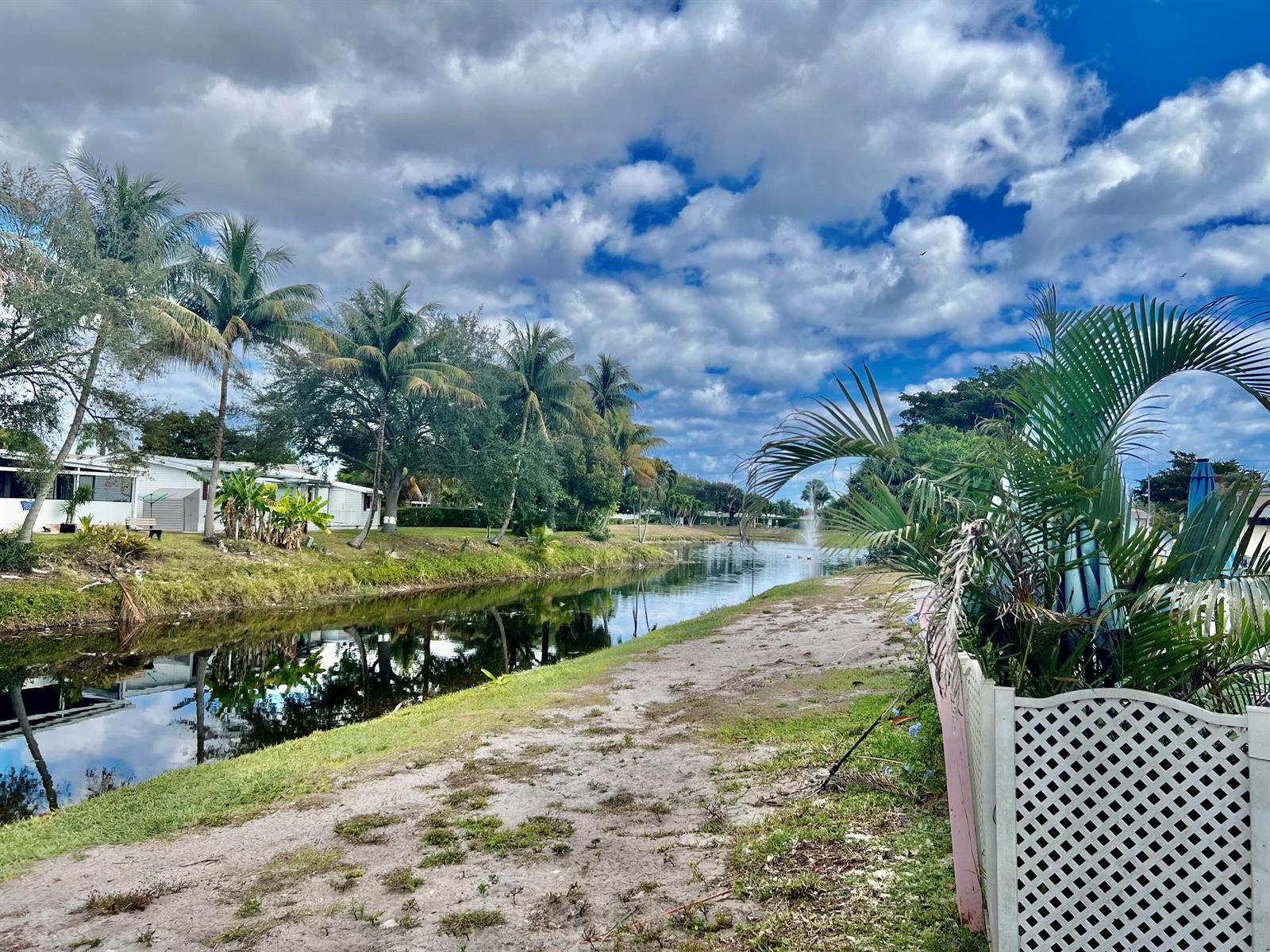 A canal flows past a grassy bank lined with palm trees and residential homes — 305 NW 50th Court, Pompano Beach FL 33064, POMPANO BEACH, FL