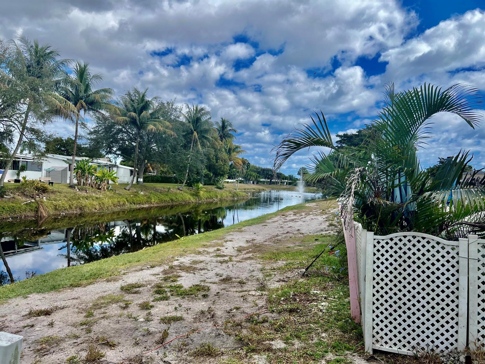 A canal flows past a grassy bank lined with palm trees and residential homes — 305 NW 50th Court, Pompano Beach FL 33064, POMPANO BEACH, FL