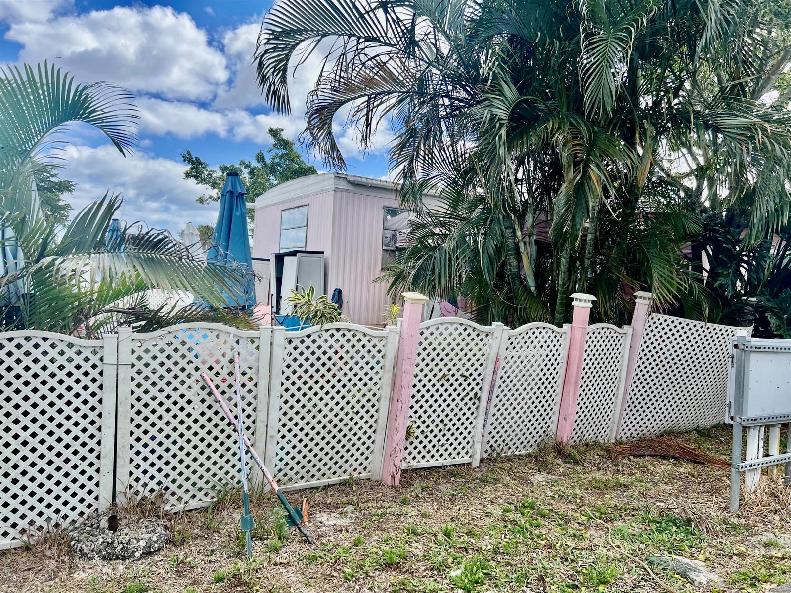 A white lattice fence stands in front of a pink mobile home and palm trees — 305 NW 50th Court, Pompano Beach FL 33064, POMPANO BEACH, FL
