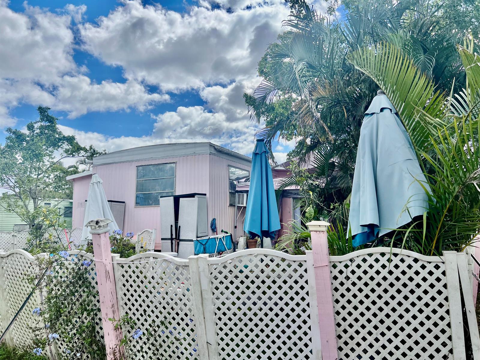 A pink mobile home exterior features a white lattice fence and two closed patio umbrellas — 305 NW 50th Court, Pompano Beach FL 33064, POMPANO BEACH, FL