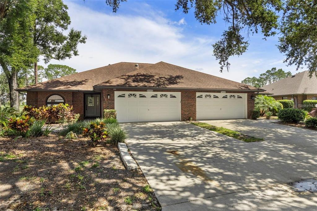 A single-story brick duplex with two white garage doors and a concrete driveway — 6549 BRENTWOOD DRIVE, ZEPHYRHILLS, FL