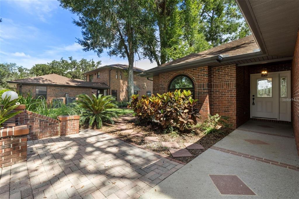 A brick house exterior features a paved walkway, a front door, and landscaped garden beds — 6549 BRENTWOOD DRIVE, ZEPHYRHILLS, FL