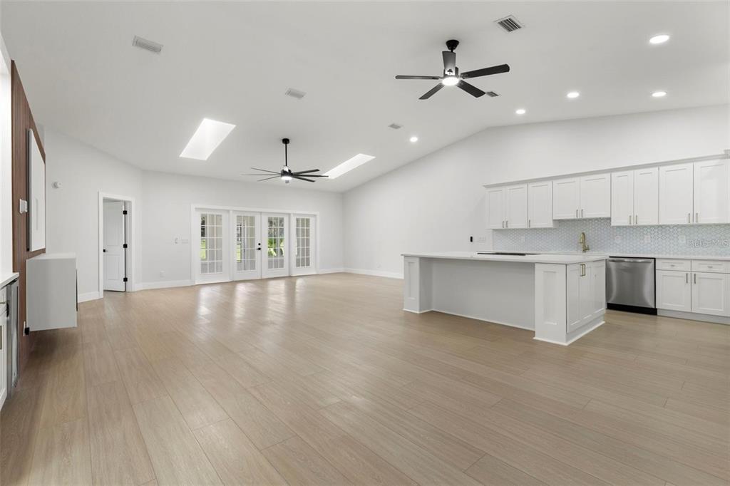 A bright, open-concept kitchen and living area features white cabinetry, a large island, and skylights — 6549 BRENTWOOD DRIVE, ZEPHYRHILLS, FL
