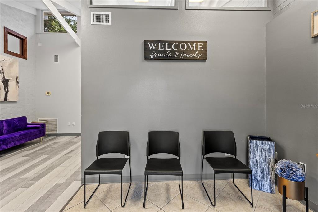 A waiting area features three black chairs against a gray wall with a welcome sign — 117 NE 1ST STREET, CHIEFLAND, FL