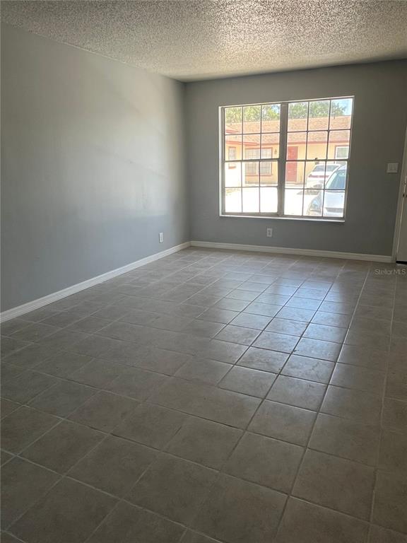An empty room with gray walls, a large window, and light-colored square floor tiles — 2009 KELLEY AVENUE, KISSIMMEE, FL