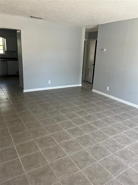 A room with light gray walls and large square floor tiles leads to a kitchen — 2009 KELLEY AVENUE, KISSIMMEE, FL