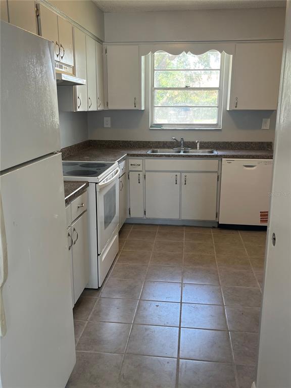 A kitchen features white cabinets, a white stove, a dishwasher, and a window above the sink — 2009 KELLEY AVENUE, KISSIMMEE, FL