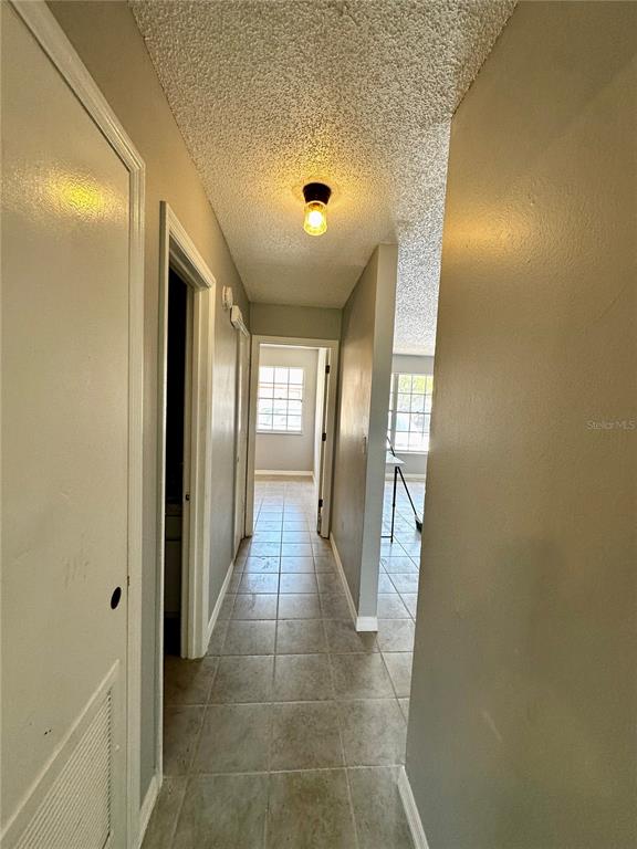 A hallway with light-colored tile flooring leads toward a room with a window — 2009 KELLEY AVENUE, KISSIMMEE, FL