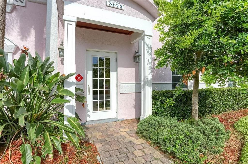 A pink house exterior features a white front door, a brick walkway, and lush landscaping — 3873 POMPANO DRIVE SE UNIT D, ST PETERSBURG, FL